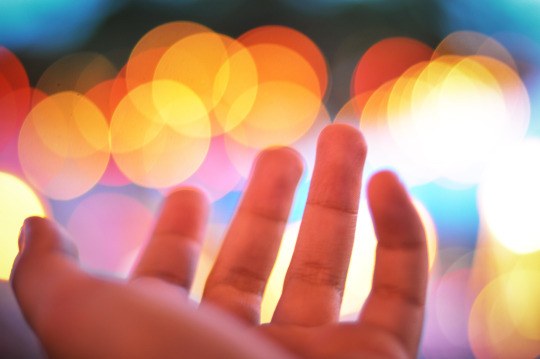 A hand reaching toward warm, out-of-focus lights